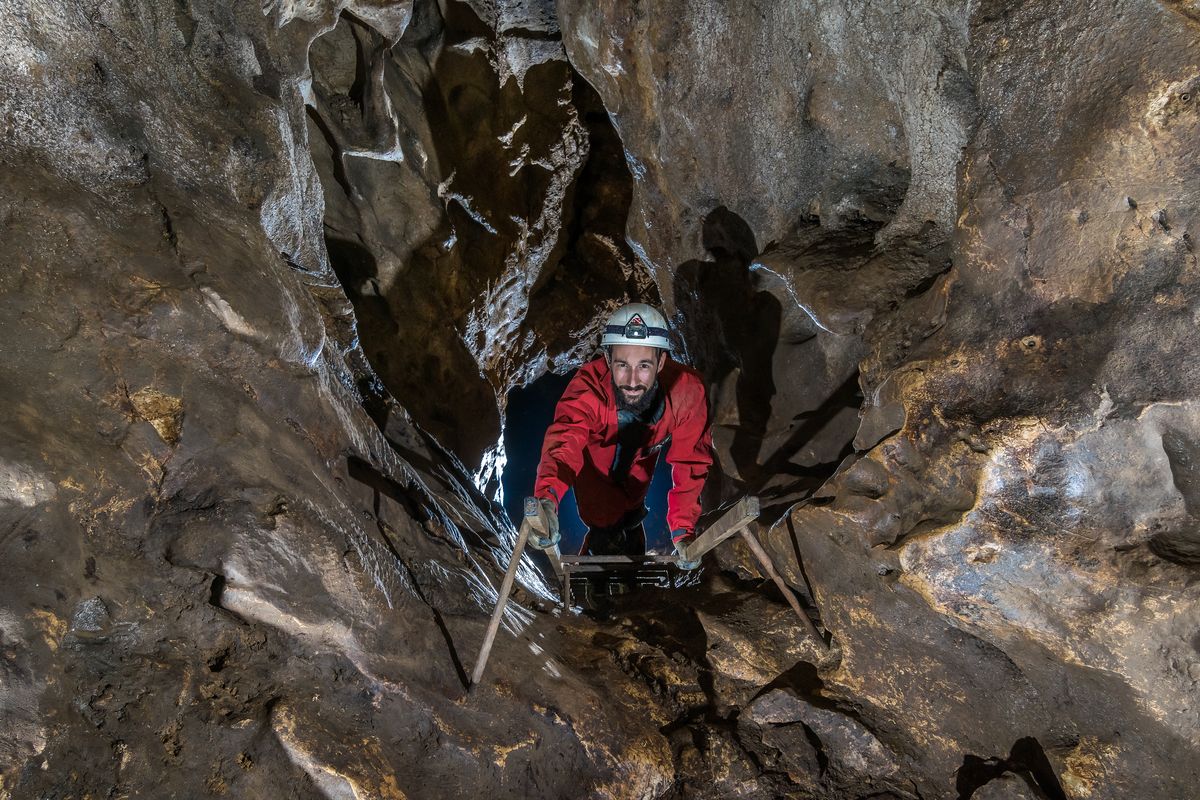 Spéléologue souriant remontant une échelle dans un passage étroit.